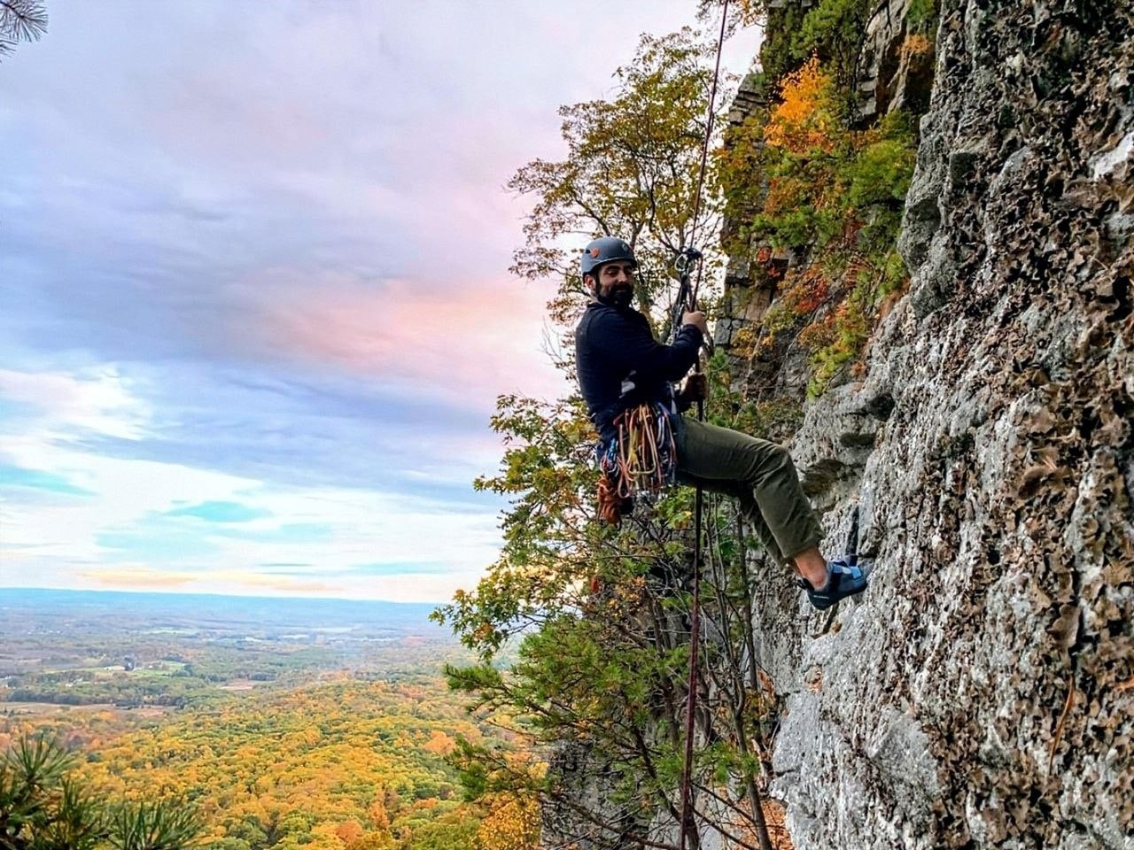 Brandon rappelling down a cliff face at sunset, an autumn valley spread out far below